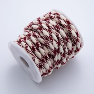 May include: Spool of decorative rope with a cream and burgundy houndstooth pattern. The rope is tightly wound around a white plastic spool. The rope is a twisted, braided design.
