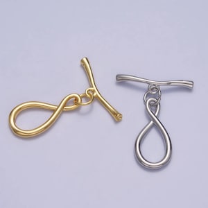 Peut inclure: Deux fermoirs à bascule en métal, l'un en or et l'autre en argent, avec un motif en forme d'infini. Les fermoirs sont utilisés pour la fabrication de bijoux.