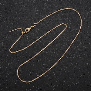 May include: A gold chain necklace with a sliding clasp. The chain is made of small, square links.