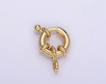 May include: A gold-colored, round jewelry clasp with a spring-loaded mechanism. The clasp features a circular body with a small ball on one end and a hinged loop on the other. The design includes decorative, rounded accents.