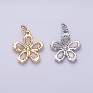May include: Two flower-shaped pendants. One is gold-toned, the other silver-toned. Each pendant has five petals, each petal containing a clear, faceted stone. The pendants have a small loop at the top for attaching to a chain or other jewelry.