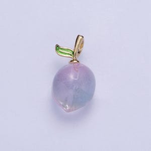 May include: A gold charm in the shape of a peach with a green leaf. The peach is made of glass and has a pink and blue iridescent finish.