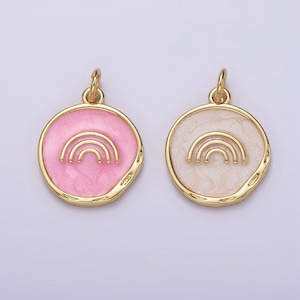 Könnte beinhalten: Zwei goldfarbene Anhänger mit einem Regenbogen-Design. Ein Anhänger hat einen rosa emaillierten Hintergrund und der andere einen weißen emaillierten Hintergrund.