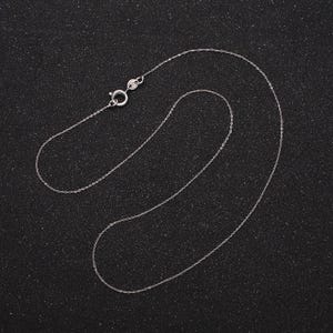 May include: A silver chain necklace with a lobster clasp closure. The chain is laid out on a black background.