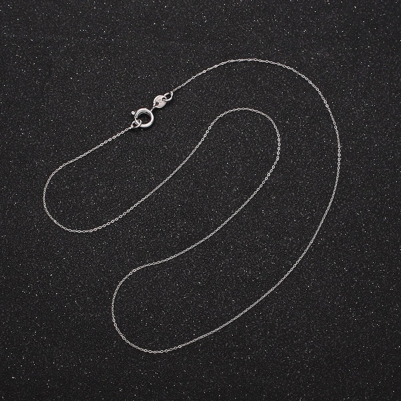 May include: A silver chain necklace with a lobster clasp closure. The chain is laid out on a black background.