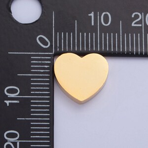 Puede incluir: Un dije de coraz&oacute;n de oro que mide aproximadamente 1 cm de ancho. El dije se muestra junto a una regla para referencia de tama&ntilde;o.