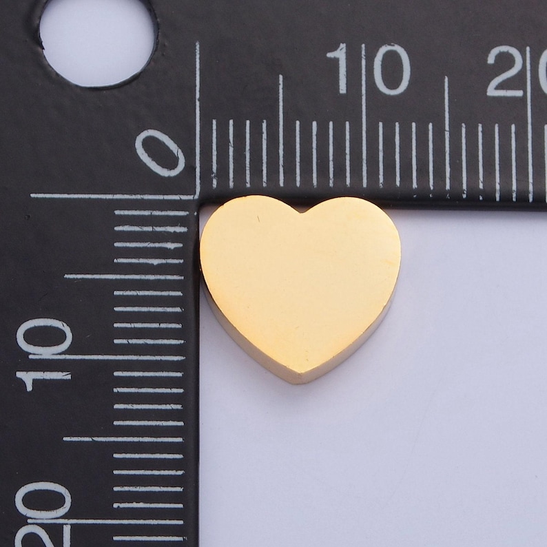 Puede incluir: Un dije de coraz&oacute;n de oro que mide aproximadamente 1 cm de ancho. El dije se muestra junto a una regla para referencia de tama&ntilde;o.