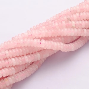 May include: Close-up of several strands of pale pink, disc-shaped beads. The beads are strung together, forming a textured, flowing pattern. The beads have a translucent quality, giving a delicate appearance. Suitable for jewellery making.