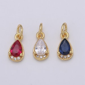 May include: Three gold teardrop-shaped pendants with different colored gemstones. The pendants have a gold bail and are adorned with small clear gemstones around the perimeter.