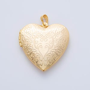 May include: A gold-colored heart-shaped locket pendant. The locket features an ornate floral design on the front and a small loop for a chain. The locket is closed with a hinge on the side.