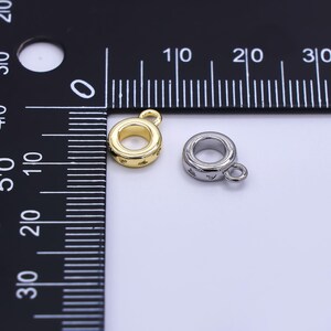 May include: Two small, round jewelry findings. One is gold-colored, the other is silver-colored. Both have a loop for attaching to other jewelry components. The gold finding has small star-shaped details around its circumference.