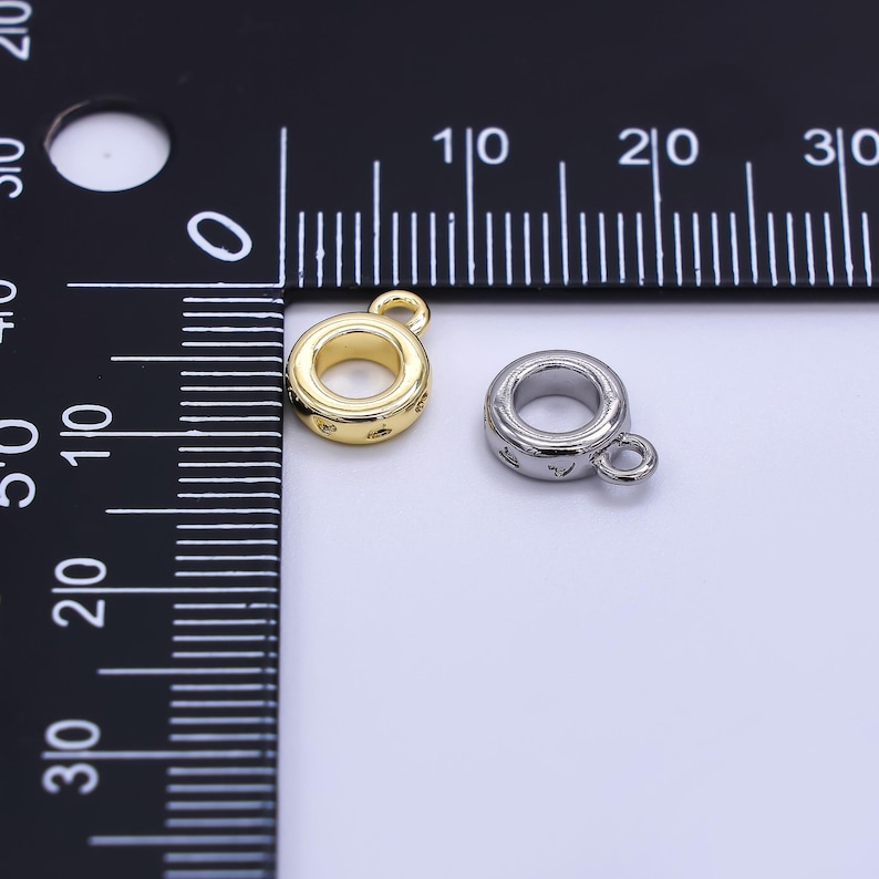 May include: Two small, round jewelry findings. One is gold-colored, the other is silver-colored. Both have a loop for attaching to other jewelry components. The gold finding has small star-shaped details around its circumference.