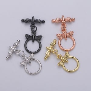 May include: Four dragonfly toggle clasps in different finishes: black, silver, gold, and rose gold. Each clasp features a detailed dragonfly design with a ring for attaching a strap or chain.