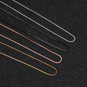 May include: Five different chain necklaces in silver, black, rose gold, gold, and a darker gold color. The chains are laid out in a row on a black background.