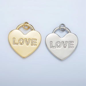 Könnte beinhalten: Zwei herzförmige Anhänger mit dem Wort "LOVE" in funkelnden Strasssteinen. Ein Anhänger ist golden und der andere silbern.