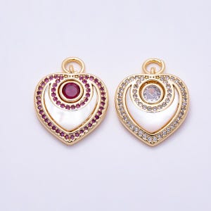 May include: Two gold-toned heart-shaped pendants with a top loop. One features a central red stone surrounded by red crystals and white inlay. The other features a central clear stone surrounded by clear crystals and white inlay.