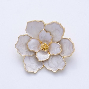 May include: A white flower brooch with gold-colored trim. The brooch has multiple petals with a marbled effect and a textured gold-colored center. The flower is set against a white background.
