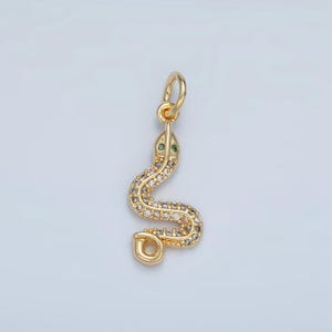 May include: A gold snake charm with clear and green gemstones. The snake is curled up with its tail in its mouth.