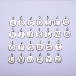 May include: A set of 26 silver charms, each featuring a letter of the alphabet, adorned with sparkling clear rhinestones. The charms are square-shaped and have a loop at the top for attaching to a necklace or bracelet.