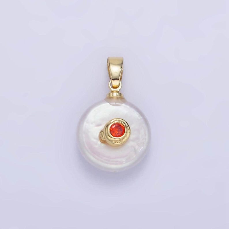 May include: A gold pendant featuring a white pearl with a small red gemstone set in the center.