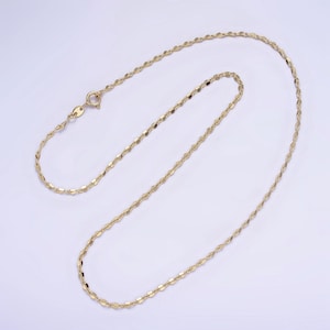 Puede incluir: Un collar de cadena de oro con un diseño delicado y trenzado. La cadena está hecha de pequeños eslabones planos que se entrelazan para crear un efecto de cuerda.