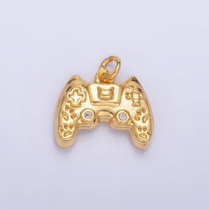May include: A gold-colored video game controller charm with clear rhinestones. The charm is detailed with a cross, a paw print, and other symbols.