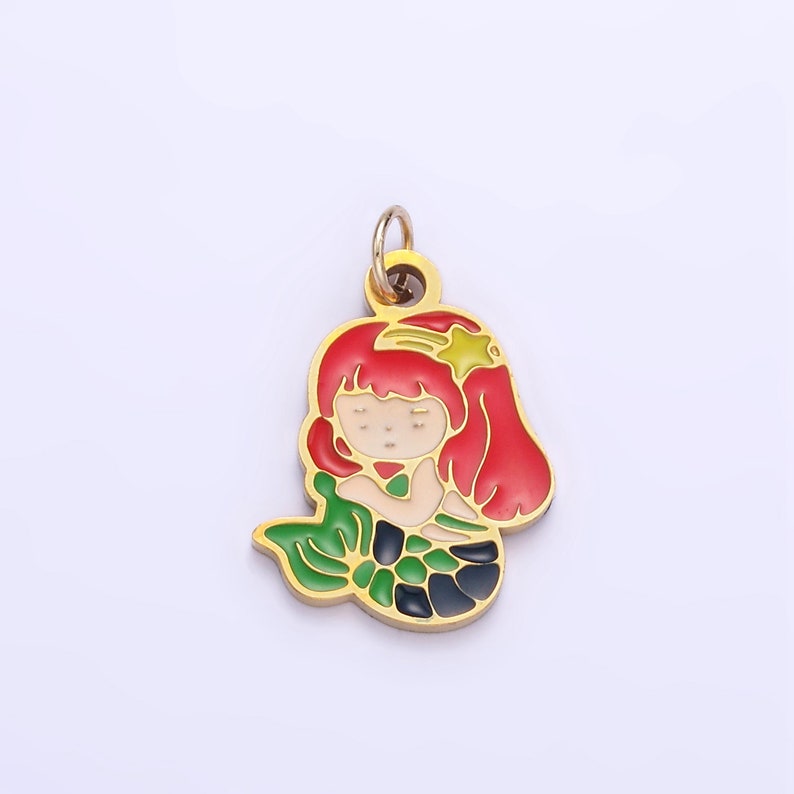 Op de afbeelding: Goudkleurige metalen hanger met een zeemeermin met rood haar, een groene staart en een gele ster op haar hoofd.