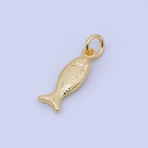 Könnte beinhalten: Ein goldfarbener Anhänger in Fischform mit strukturierter Oberfläche. Der Anhänger hat oben eine Schlaufe zum Befestigen an einer Kette oder einem Armband. Der Fisch hat eine detaillierte Flosse und einen Schwanz.