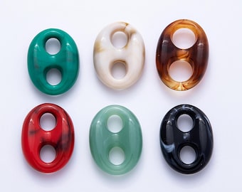 Puede incluir: Seis cuentas ovaladas en varios colores: verde, blanco roto, marrón, rojo, verde claro y negro con vetas blancas. Cada cuenta tiene dos agujeros circulares. Las cuentas están dispuestas sobre una superficie blanca.