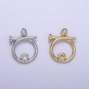 May include: Two silver and gold nail charm pendants with a clear rhinestone in the center. The nail is wrapped around a circle.