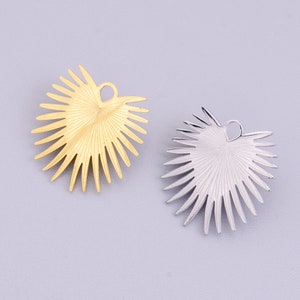 Op de afbeelding: Twee metalen palmblaadjes, een gouden en een zilveren, met een gat aan de bovenkant om aan sieraden te bevestigen.