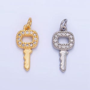May include: Two key-shaped charms with a square head, one gold and one silver, both with clear rhinestones around the edges.