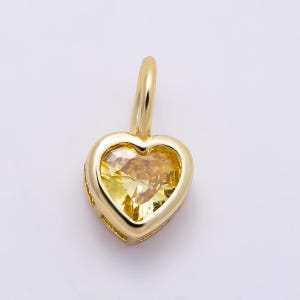 May include: A gold pendant featuring a heart-shaped yellow gemstone set within a polished gold frame. The pendant includes a small, rounded gold bail at the top for attachment, showcasing a faceted cut that reflects light across the yellow stone.