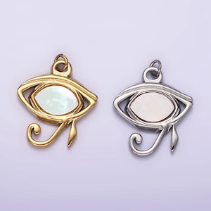 Puede incluir: Dos colgantes de oro y plata en forma de Ojo de Horus con una incrustación de nácar blanco.