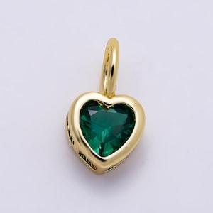 May include: A heart-shaped pendant featuring a faceted deep green gemstone set within a polished gold-toned metal frame. The pendant includes a small, smooth gold-toned bail at the top for attachment to a chain, showcasing a clean, reflective finish.