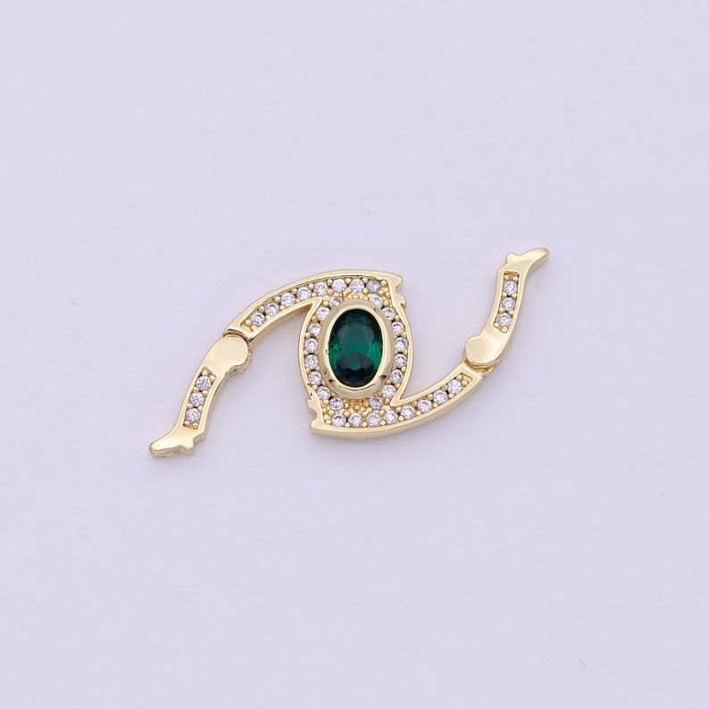 May include: Gold-tone eye-shaped clasp with a green gemstone surrounded by clear rhinestones.