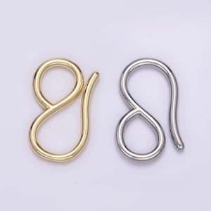 May include: Two metal hook clasps, one gold-toned and one silver-toned, are displayed against a light background. Each clasp has a looped design with a curved hook, suitable for jewelry making or crafting projects.