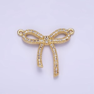 May include: Gold-tone bow charm with clear crystal embellishments. The bow has a loop at the top for attaching to a necklace or bracelet.