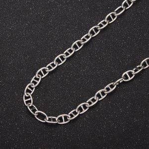 Puede incluir: Un collar de cadena de plata con un diseño de eslabón marinero. La cadena está sobre un fondo negro.