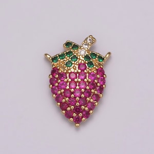 May include: A gold-toned strawberry pendant with a vibrant design. The body is composed of numerous magenta-colored stones, while the leaves are green. A single white stone accents the top. This jewelry piece is suitable for necklaces or bracelets.