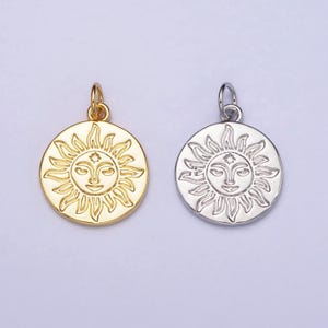 May include: Two sun charm pendants, one gold and one silver, with a detailed sun face design. The sun has a smiling face with a star in the center of its forehead.