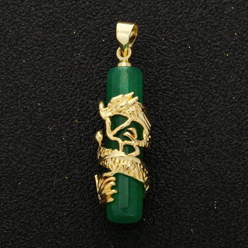 Op de afbeelding: Een gouden hanger met een groene jade-steen die is gegraveerd met een drakenontwerp. De hanger is op een zwarte achtergrond.