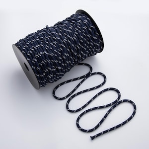 May include: A spool of navy blue rope with a white reflective pattern. The rope is coiled on a black spool, with a length of rope unraveled and laid out. The rope is suitable for crafting, nautical projects, or general use.