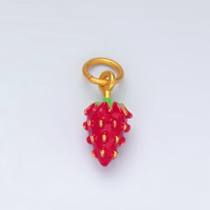 May include: A gold charm shaped like a strawberry with a red body and green leaves. The charm has a gold loop at the top for attaching to a bracelet or necklace.