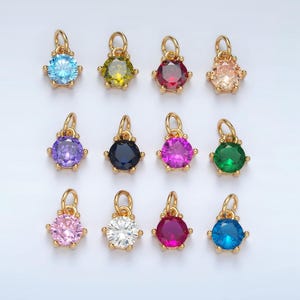 Pode incluir: Doze pingentes de ouro com pedras preciosas de diferentes cores. Cada pingente apresenta uma pedra preciosa redonda cercada por uma moldura de ouro. As pedras preciosas são azuis, verdes, vermelhas, rosas, roxas, pretas, brancas e transparentes.