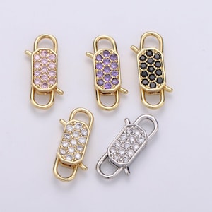 May include: Five gold-tone metal clasps with different colored crystal accents. The clasps are rectangular with a rounded top and bottom. The crystals are set in a grid pattern. The clasps are for jewelry making.