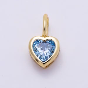 May include: A heart-shaped pendant featuring a faceted light blue gemstone set in a polished yellow gold frame. The pendant includes a small, smooth yellow gold bail at the top, designed for attachment to a necklace chain or cord.