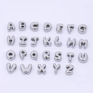 May include: A collection of shiny, silver alphabet letter charms. Each letter is in a rounded, bubble-like font. The letters are arranged in rows, showcasing the entire English alphabet from A to Z.