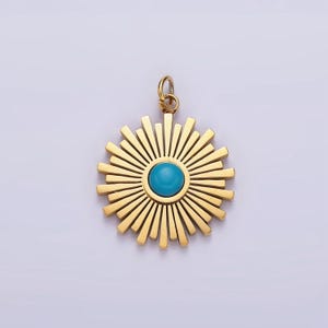 Könnte beinhalten: Ein goldfarbener Anhänger mit Sonnenstrahlen-Design. Der Anhänger hat einen zentralen, runden, türkisfarbenen Stein. Das Sonnenstrahlen-Design hat mehrere Strahlen, die sich vom Zentrum aus erstrecken. Der Anhänger hat oben eine kleine Schlaufe für eine Kette.