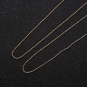 Peut inclure: Deux chaînes en or avec un design perlé sur un fond noir.